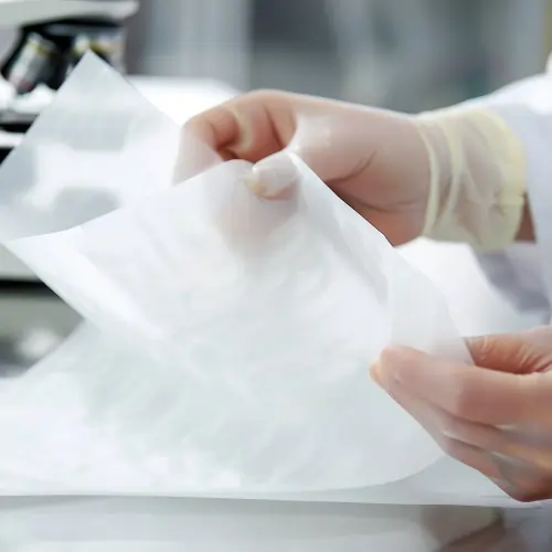 Gloved hands holding sterile paper products sheet in a laboratory setting