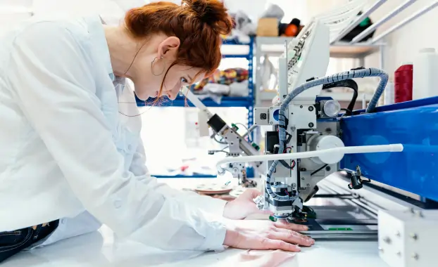 Close-up of a technician operating a computerized sewing machine for textile quality and durability testing.