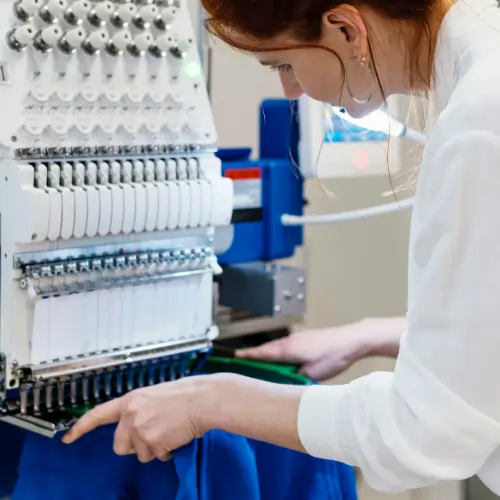 Close-up of a technician inspecting fabric during textile durability testing on a multi-needle embroidery machine.